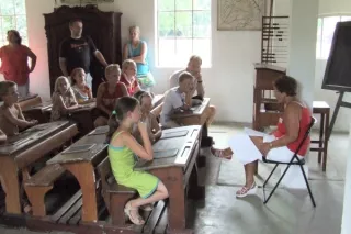 Kinderen in ouderwetse schoolbanken, met juf voor de klas
